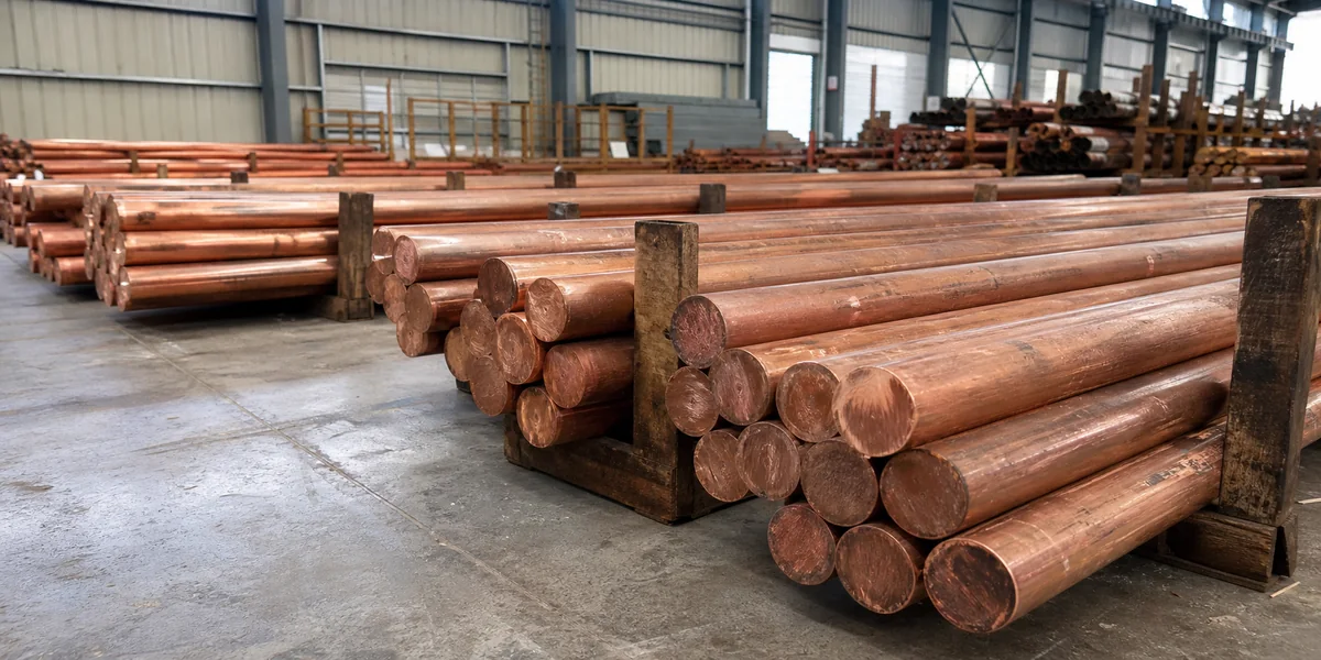 Reddish copper round rods stored on timber racks in a bright metal warehouse