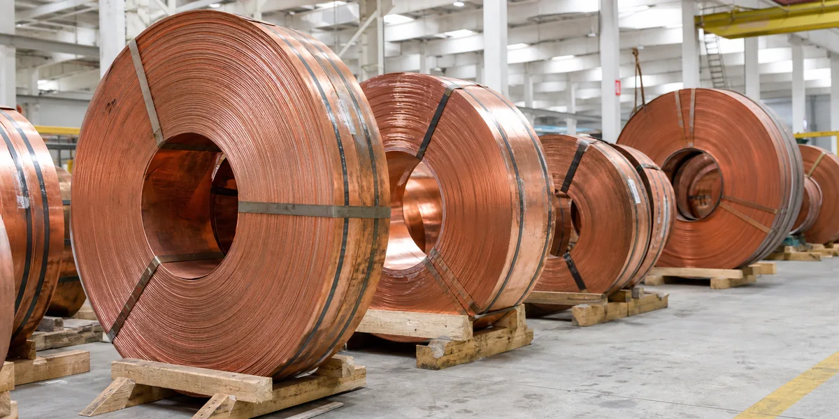 Reddish copper strip coils secured on timber cradles in a bright warehouse